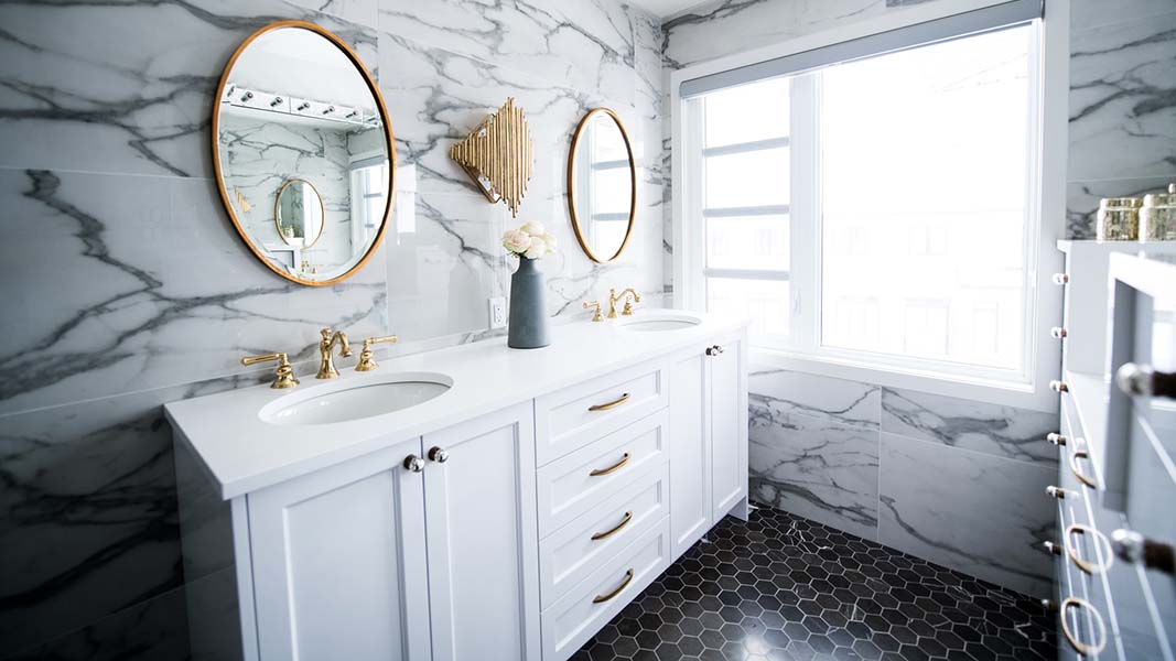 luxury bathroom with marble white tiles and white vanity, gold framed round mirrors on the wall